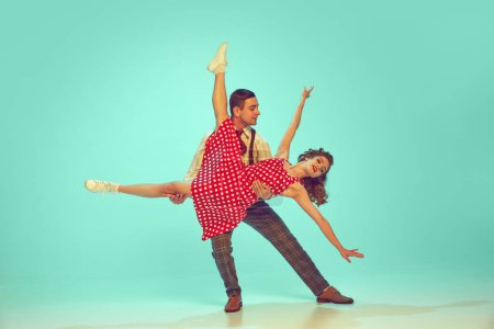 Swing-Tänzer strahlen Fröhlichkeit aus, während sie vor Mint-Hintergrund energiegeladene Tanzbewegungen vollführen. Konzept von Musik, Hobby, Kunst, Energie, Glück, Stimmung, Aktion, Kultur der 60er, 70er Jahre