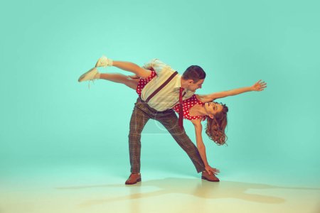 Swing dancers radiating happiness while performing energetic dance moves in motion against gradient mint background. Concept of music, hobby, art, energy, happiness, mood, action, 60s, 70s culture