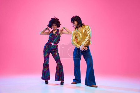Talentierte Tänzer, Männer und Frauen in Retro-Outfits posieren vor rosa Studiohintergrund. Konzept der amerikanischen Kultur, Mode der 1970er, 1980er Jahre, Musik, Epochenvergleiche.