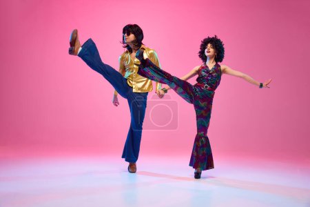 Disco Dreams. Dance duo, man and woman in retro fashion outfit dancing in motion against gradient pink studio background. Concept of American culture, 1970s, 1980s fashion, music, comparisons of eras.