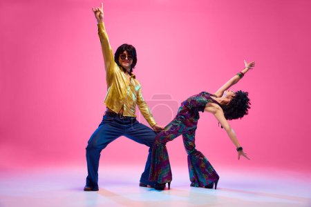 Disco Dreams. Dance duo, man and woman in retro fashion outfit dancing in motion against gradient pink studio background. Concept of American culture, 1970s, 1980s fashion, music, comparisons of eras.
