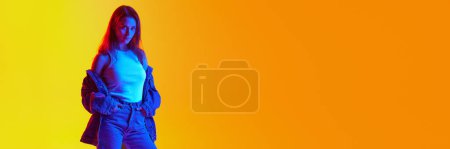 Banner. Young confident woman in style denim-casual outfit against gradient studio background in mixed neon light. Negative space to insert text. Concept of human emotions, self-expression, youth. Ad