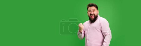 Banner. Young smiling man rejoice success and clenched fist against vibrant green studio background. Negative space to insert text. Concept of human emotions, self-expression, success in work.