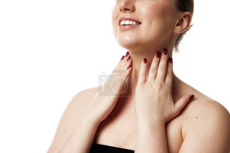 Téléchargez les photos : Portrait recadré de femme au sourire radieux touchant son cou montrant des soins de la peau efficaces sur fond de studio blanc. Concept de beauté naturelle personnes, injections, procédures de spa, cosmétologie. Publicité - en image libre de droit