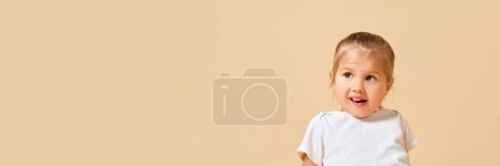 Banner. Portrait of cute, playful little girl looking away against beige studio background with negative space to insert text. Concept of childhood, motherhood, life, birth. Copy space for ad