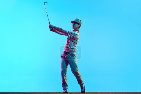 Full length portrait of golfer hitting golf shot with club on course in neon light against gradient blue background. Concept of professional sport, luxury games, active lifestyle, action. Ad