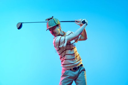 Jugador de golf en campo de golf profesional. Golfista en traje retro con palo de golf tomando tiro en luz de neón contra el fondo azul degradado. Concepto de deporte, juegos de lujo, estilo de vida activo, acción. Anuncio