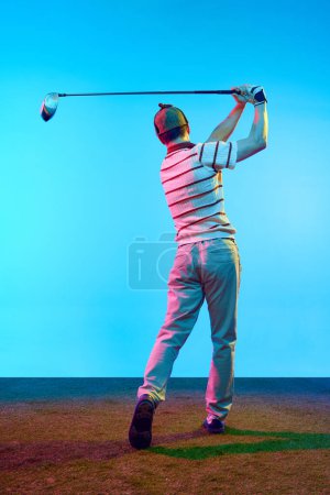 Retrato vista trasera de golfista en traje retro con palo de golf tomando tiro en luz de neón contra el fondo azul degradado. Concepto de deporte profesional, juegos de lujo, estilo de vida activo, acción. Anuncio