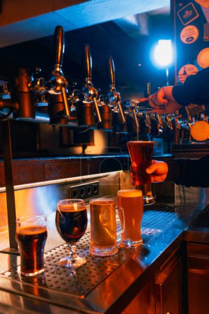 Téléchargez les photos : Barman main remplissage grand verre avec de la bière noire à côté de la sélection d'autres styles de bière. Servant de la bière artisanale du robinet. Concept de boissons alcoolisées, vie nocturne, fête, festivals, Oktoberfest. Publicité - en image libre de droit
