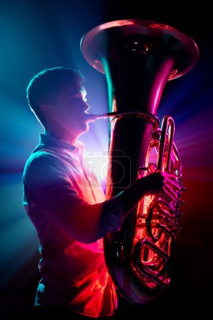 Silhouette eines künstlerischen, talentierten Musikers, Trompeters, der seine neue Symphonie im Neonlicht vor schwarzem Hintergrund aufführt. Konzept von Hobby und Arbeit, Musikfestivals, Konzerten, Symphoniekonzerten, Kultur.