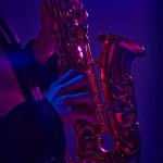 Cropped photo of talented solo player performing on saxophone in vibrant pink neon light against dark studio background. Concept of music and art, hobby, concerts and festivals, modern culture. Ad