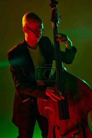 Photo for Portrait of bald musician in glasses plays double bass in red-green neon light against gradient studio background. Concept of music and art, hobby, concerts and festivals, modern culture. Ad - Royalty Free Image