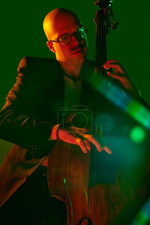 Foto de Hombre calvo, talentoso violonchelista interpretando composiciones de jazz en luz de neón rojo-verde contra el degradado fondo del estudio. Concepto de música y arte, hobby, conciertos y festivales, cultura moderna. Anuncio - Imagen libre de derechos