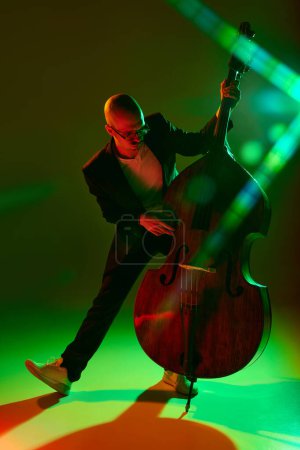 Foto de Talentoso violonchelista interpretando composiciones de jazz en luz de neón rojo-verde sobre fondo de estudio degradado. Concepto de música y arte, hobby, conciertos y festivales, cultura moderna. Anuncio - Imagen libre de derechos
