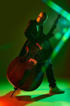 Photo for Bald musician playing double bass in red-green neon, stage light against gradient studio background. Concept of music and art, hobby, concerts and festivals, modern culture. Ad - Royalty Free Image
