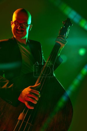 Contemporary double bass player in silhouette in red-green neon light against gradient studio background. Concept of music and art, hobby, concerts and festivals, modern culture. Ad
