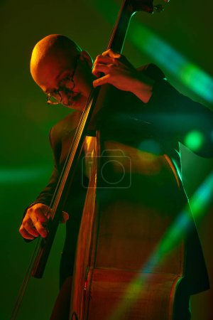 Photo for Talented musician playing jazz on double bass in red-green neon, stage light against gradient studio background. Concept of music and art, hobby, concerts and festivals, modern culture. Ad - Royalty Free Image