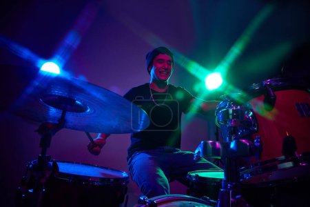 Photo for Overjoyed stylish drummer performing in pink-purple stage lighting against gradient studio background. Concept of music and art, hobby, concerts and festivals, modern culture. Ad - Royalty Free Image