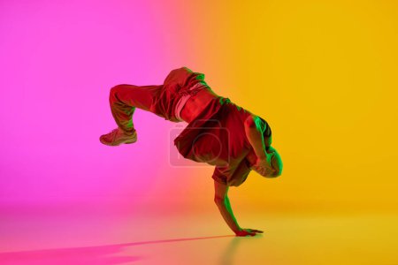 Photo for Young man dancing in freestyle, training moves in motion in neon light against gradient pink-yellow background. Concept of art, hobby, sport, creativity, fashion and style, action. Ad - Royalty Free Image
