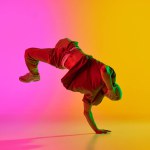 Young man dancing in freestyle, training moves in motion in neon light against gradient pink-yellow background. Concept of art, hobby, sport, creativity, fashion and style, action. Ad
