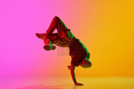 Photo for Dynamic photo of young, talented man dancing breakdance moves in neon light against gradient pink-yellow background. Concept of art, hobby, sport, creativity, fashion and style, action. Ad - Royalty Free Image
