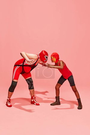 Middle-aged man with little boy stands in attack pose and looking to each other with angry emotions against pink studio background. Concept of pop art, difference, costume festivals, competitions. Ad