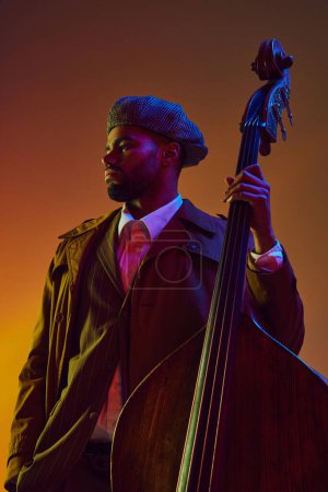 Téléchargez les photos : Portrait d'homme afro-américain, joueur à l'expression sereine posant avec instrument à cordes au néon sur fond dégradé. Concept d'art, de musique, de musique classique et de style de vie moderne. Publicité - en image libre de droit