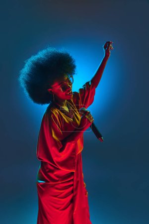 Photo for Talented African-American woman, jazz singer dancing and singing in neon light against gradient background. Concept of art, music, hobby, classical music and modern lifestyle. Ad - Royalty Free Image