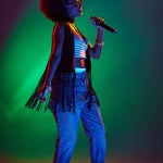 Professional vocalist with stylish afro hair performing jazz songs in neon stage light against gradient background. Concept of art, music, hobby, classical music and modern lifestyle. Ad