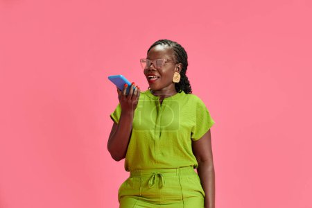 Portrait of young African-American woman talking on phone in red neon light against pastel pink studio background. Concept of human emotions, fashion and beauty, trends, communication.