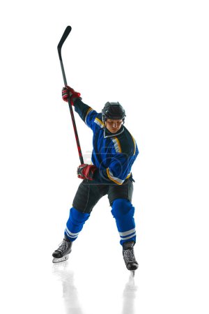 Prêt à attaquer, joueur de hockey athlétique, préparé et concentré, glisse avec un bâton tenu haut sur fond de studio blanc. Concept de sport professionnel, compétition, mouvement, tournoi, match. Publicité