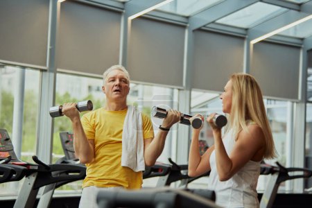 Photo for Mature couple, man and woman in sportswear doing exercises for hands with dumbbells in modern gym. Concept of sport, active seniors in modern life, healthy lifestyle, fitness centers for retirements. - Royalty Free Image