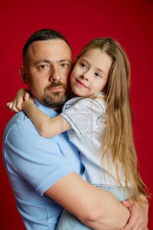 Photo for Portrait of young man holds on hands his beloved little daughter against vibrant red studio background. Fathers love Concept of Fathers day. Childrens day, Family day, parenthood. Ad - Royalty Free Image