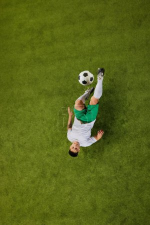 Aerial shot of soccer player in mid-air performing acrobatic kick, with ball suspended above green field. Concept of professionals sport, competition, tournament, energy, action. Ad