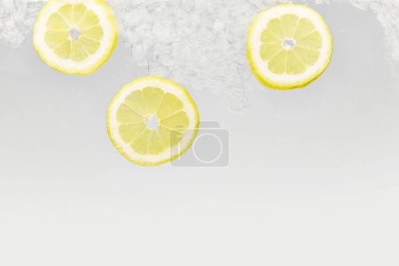 Close up shot of slices of lemon with ice floating in glass of water. Refreshing and detoxed drinks. Textured photo. Abstract wallpaper. Concept of food and drinks, summer,vitamins, nutrition.
