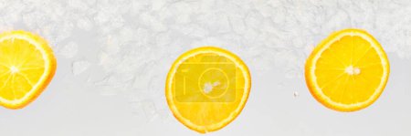 Banner. Slices of citrus, sweet and sour orange float in clear water with ice cubes against white background. Abstract wallpaper. Concept of food and drinks, summer,vitamins, nutrition.