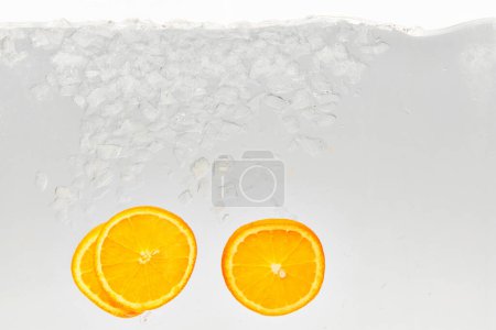 Textured photo of glass of water with ice in which add slices of sweet and sour citrus fruit, orange. Abstract wallpaper. Concept of food and drinks, summer,vitamins, nutrition.