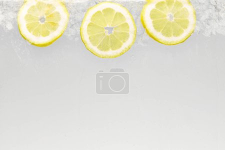 Close up shot of slices of lemon with ice floating in glass of water. Refreshing and detoxed drinks. Textured photo. Abstract wallpaper. Concept of food and drinks, summer,vitamins, nutrition.
