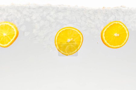 Textured photo. Slices of citrus, sweet and sour orange float in clear water with ice cubes against white background. Abstract wallpaper. Concept of food and drinks, summer,vitamins, nutrition.