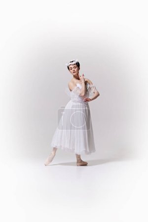 Im klassischen weißen Ballettkostüm posiert zarte Ballerina, die Anmut und Weiblichkeit vor weißem Studiohintergrund verkörpert. Kunstbegriff, Verschmelzung von Klassik und Moderne, Anmut und Eleganz.