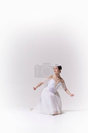 Poster. Ballerinas white gown and floral headpiece accentuate her ethereal presence against white studio background. Concept of art, fusion of classic and modernity, grace and elegance.