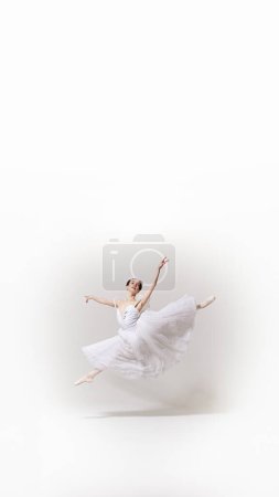 Plakat. Ballerina in weißem Kleid, fließendem Tutu führt Ballettsprung vor weißem Studiohintergrund mit negativem Raum zum Einfügen von Text aus. Kunstbegriff, Verschmelzung von Klassik und Moderne, Anmut. Anzeige