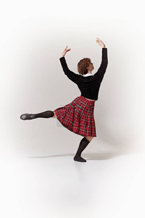 Bailarina de ballet vestida con el atuendo tradicional escocés como un personaje fantástico y actuando en movimiento contra el fondo blanco del estudio. Concepto de arte, fusión de clásico y modernidad, gracia, elegancia.