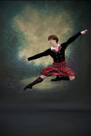 Young man in traditional Scottish outfit strikes graceful pose jumping in mid-air. Dancer in scene of famous performance against vintage style background. Concept of fusion of classic and modernity
