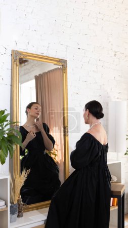 Portrait of young attractive mature woman looks at mirror with reflection of beautiful young woman, blending present and future selves. Concept of past and future, generation, memories, female beauty