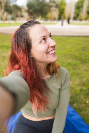 Mujer sonriendo y mirando hacia otro lado mientras se toma una selfie en el parque.