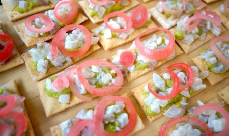 Gourmet crackers topped with avocado and pickled onion on a wooden board.