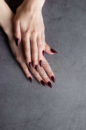 Schöne Hände einer jungen Frau mit dunkelroter Maniküre auf Nägeln auf dunklem Hintergrund