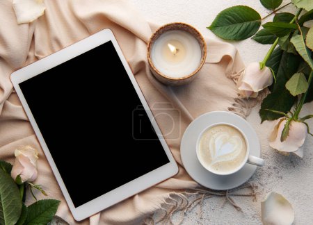 Photo for Minimalist workspace with digital tablet empty screen mockup, cozy scarf, a cup of coffee and roses flowers on concrete background. Top view, flat lay - Royalty Free Image