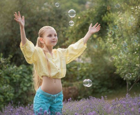 Foto de Beautiful little girl catches soap bubbles in a field with lavender - Imagen libre de derechos